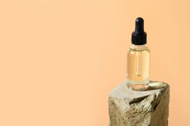 Beauty cosmetic oil in glass bottle on stone podium on beige. Space for design or text.